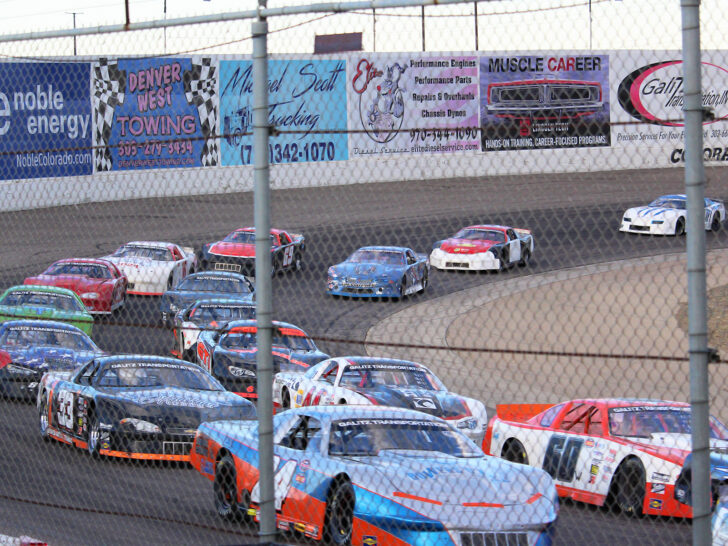 race cars driving around track with fence in foreground