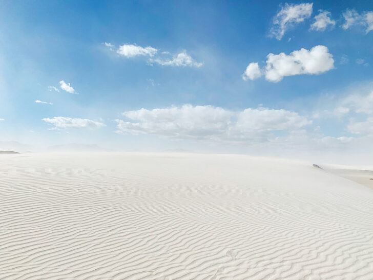 white sand dune with waves and blue sky with clouds