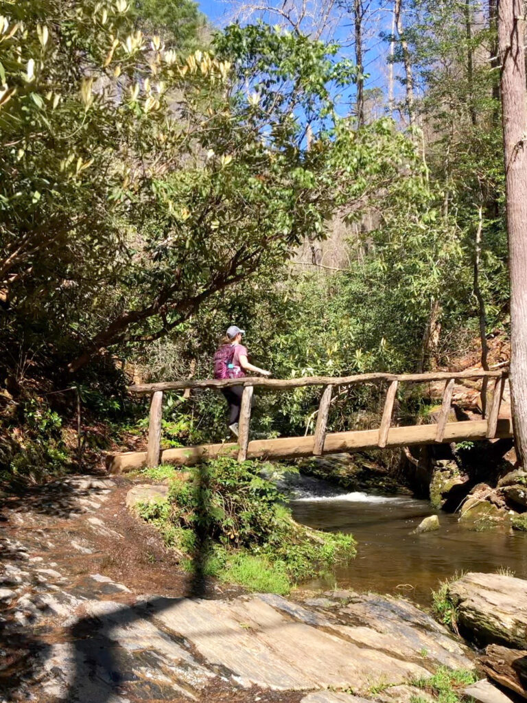 woman on bridge over stream with trees along waterfall hikes smoky mountains