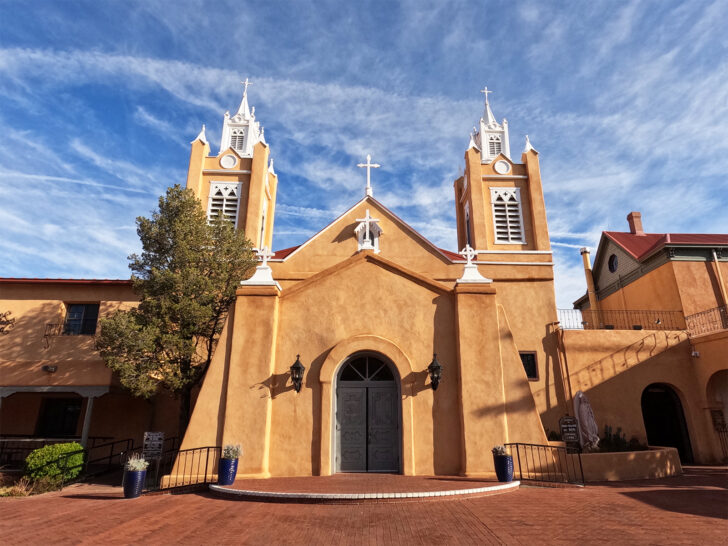 best places to travel in august USA view of orange stucco church with wispy clouds up above