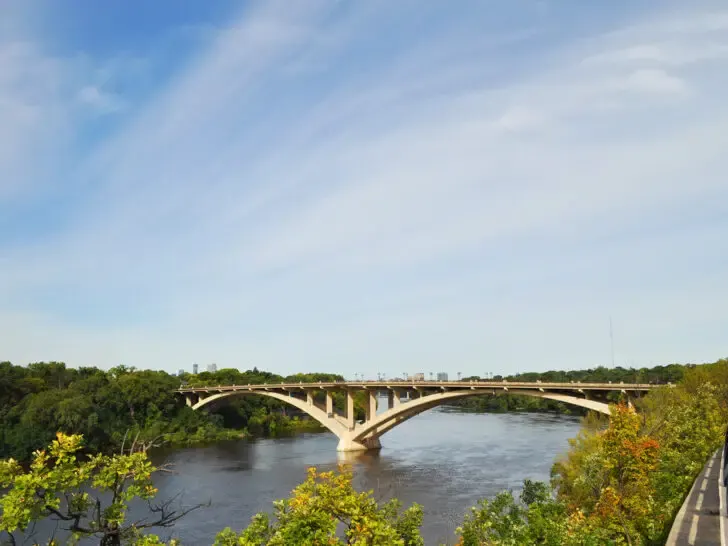 best vacations in august view of trees and river with arch bridge and clouds in sky