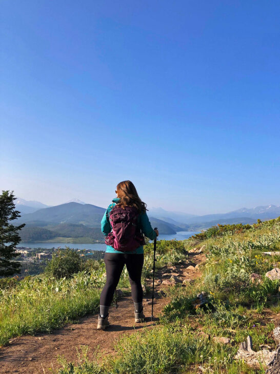 woman hiking on trail in Colorado with purple backpack and green jacket black pants
