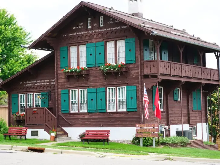 unique places to visit in August USA view of building in New Glarus Wisconsin with teal shutters flowers and brown siding