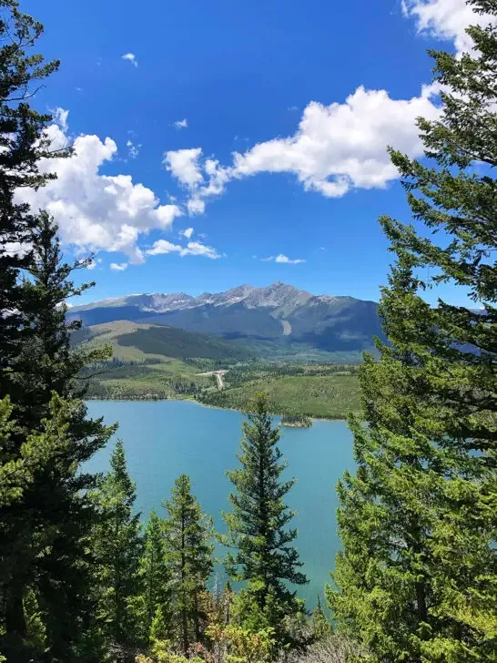 best colorado hikes view of blue lake through trees with mountain in distance