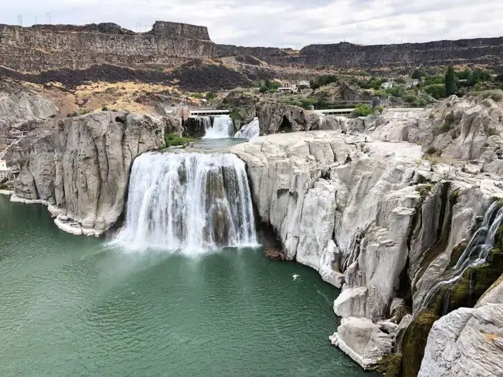 water falling over rocky shoreline into river below with cliffside in distance