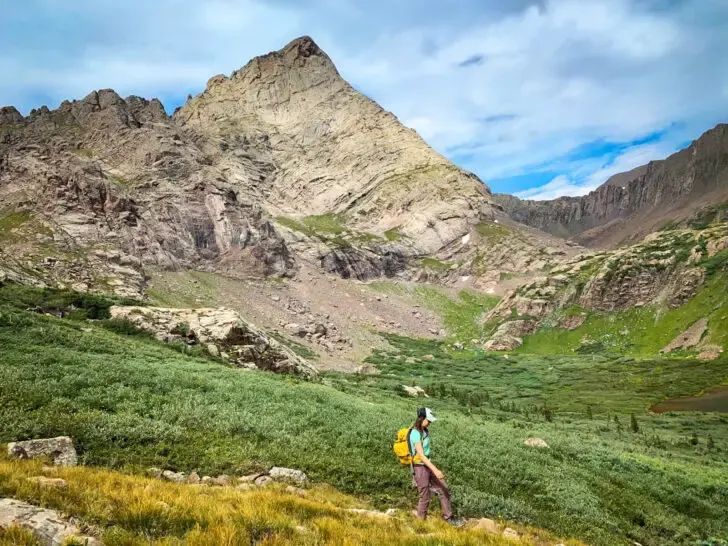 Colorado hiking trails with mountains and green meadow and person hiking in foreground