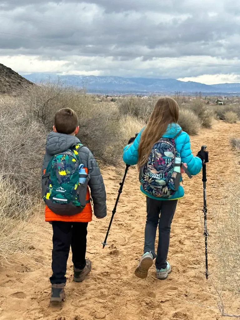 Denver to Albuquerque drive two kids on trail with hiking backpacks coats and trekking poles with mountains in distance