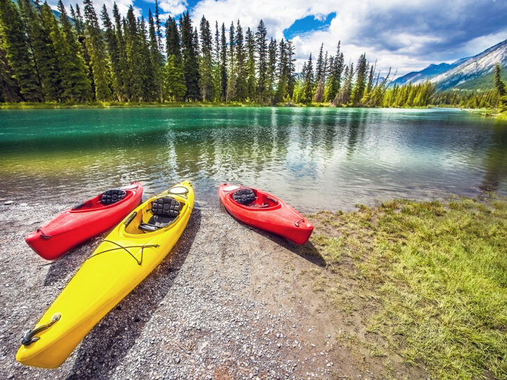 Banff in summer with red and yellow kayak on river bank with trees and lake
