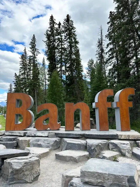Banff summer vacation view of large brown letter BANFF sign with trees behind it