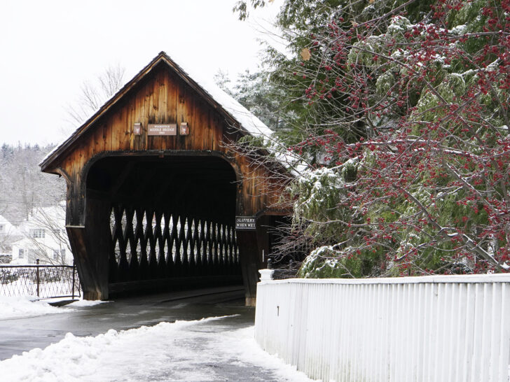 best places to visit in November view of snowy road with covered bridge and fence with red berry bush
