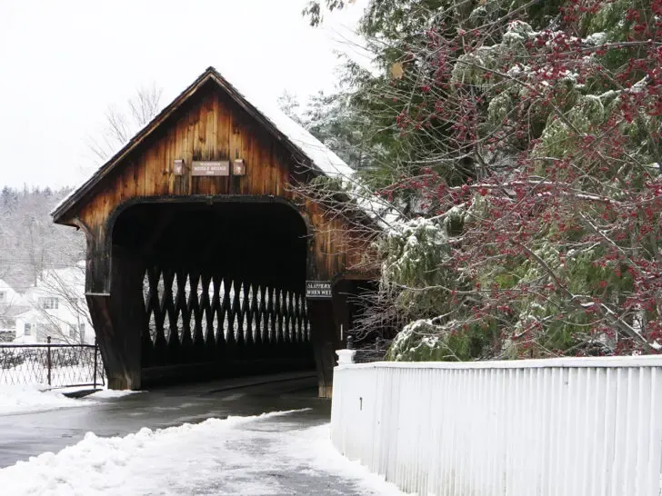 best places to visit in November view of snowy road with covered bridge and fence with red berry bush