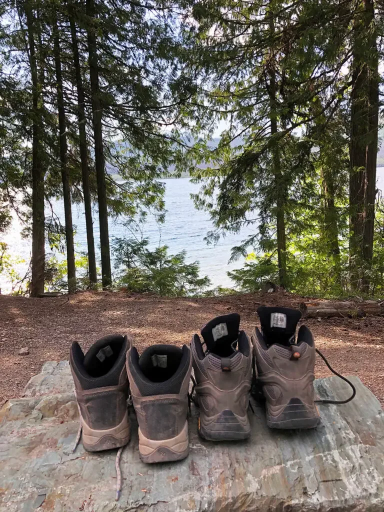 two pairs of hiking boots on rock near lake and trees