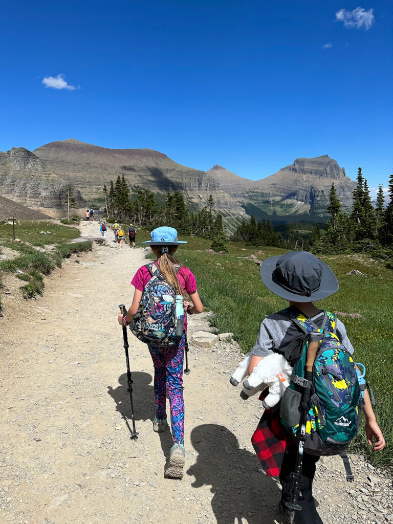 kids wearing hiking hats and backpacks and poles on trail with mountains