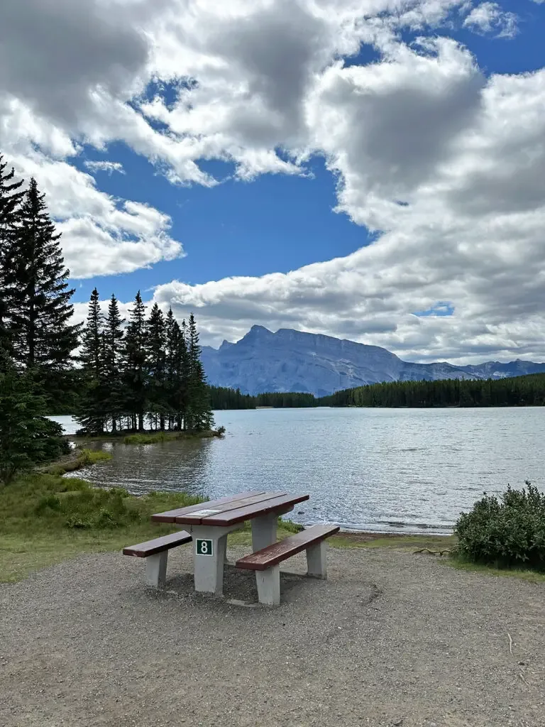 picnic table at lake edge with white puffy clouds