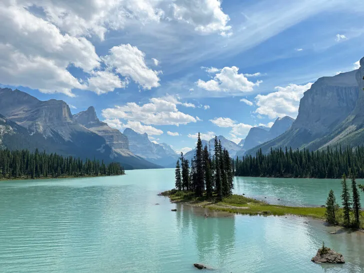view of bright teal water with island and mountains on a banff jasper road trip