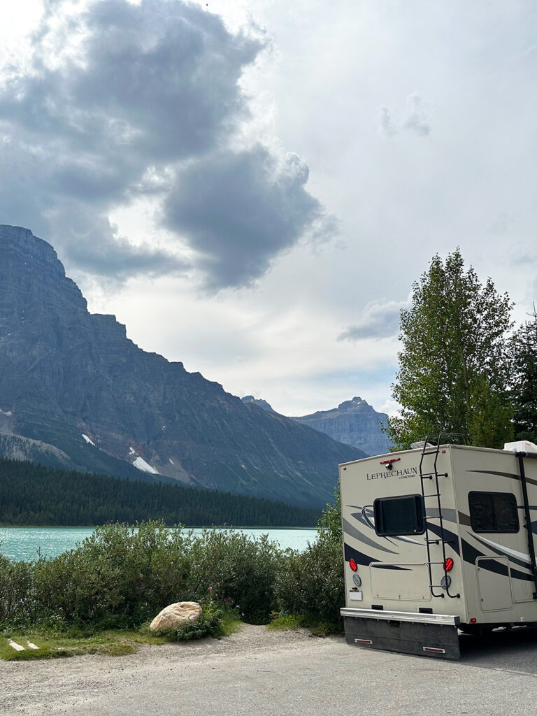 RV parked on side of road and lake with mountain