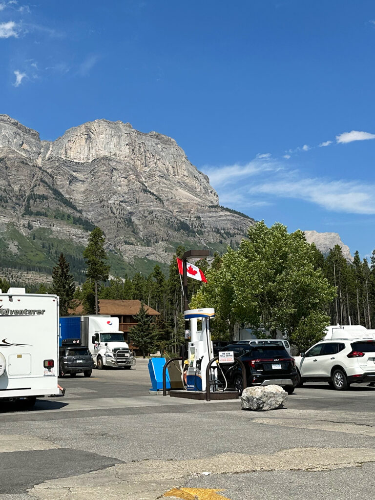 banff to jasper view of gas station with cars Canadian flag and mountains in distance