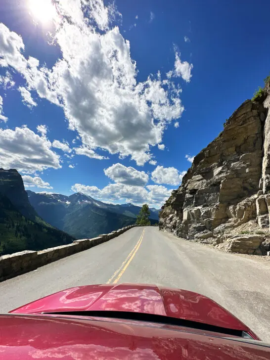 car driving down going to the sun road in glacier national park with mountains in distance