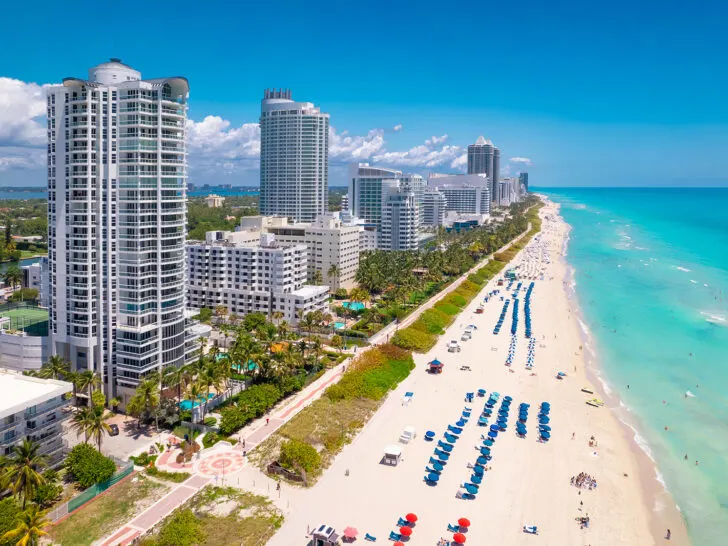 aerial view of beach with colorful umbrellas tall skyscrapers and teal water warm winter destinations