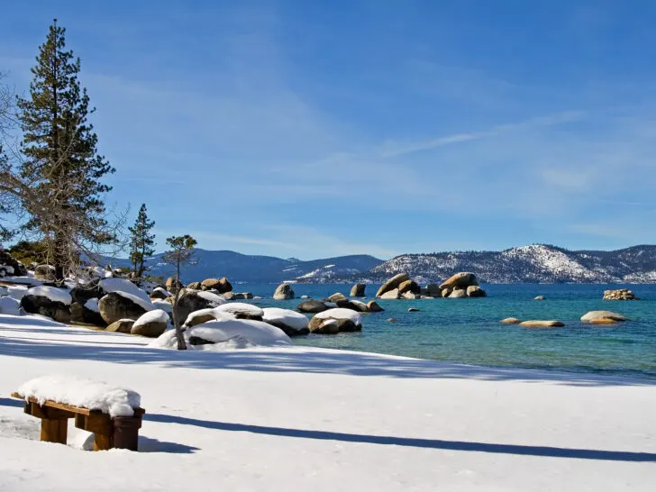 vivid color lake with trees and snowy covered rocks and mountains in distance