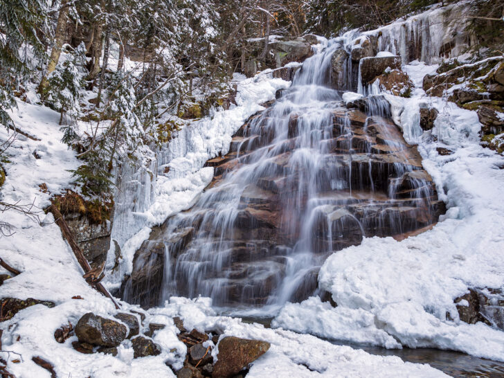 waterfall in snowy mountain scene during a winter road trip through New Hampshire