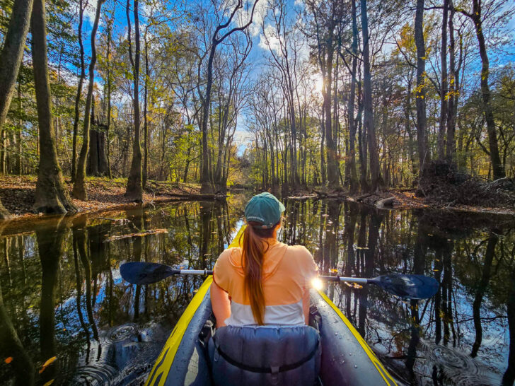 best national parks to visit in March with woman sitting in front of kayak with tall trees and river