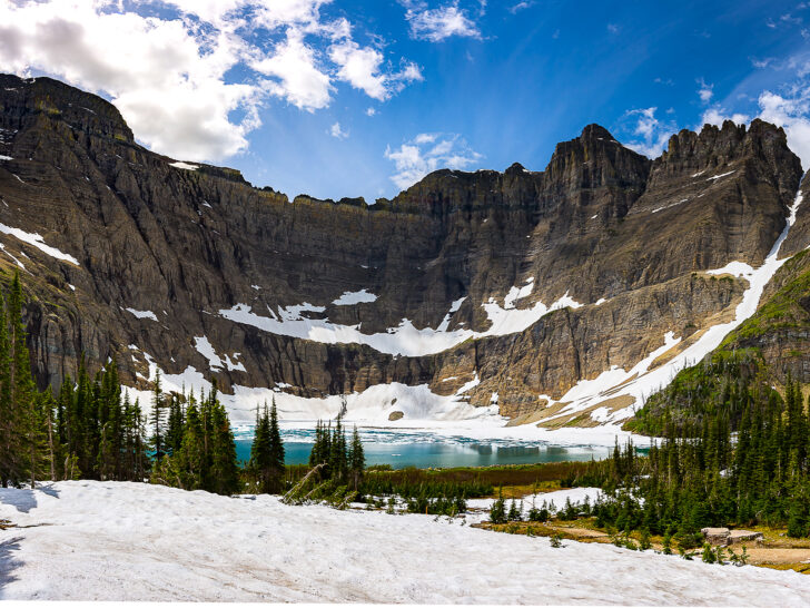 Iceberg Lake with mountain backdrop and snow and trees in the foreground