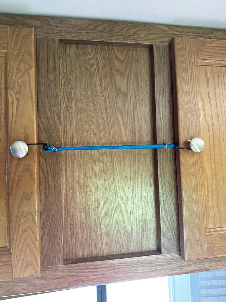 blue bungee cord holding together cabinet doors for safety