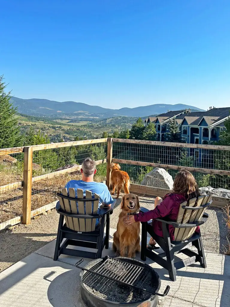 man and woman sitting with two dogs with mountains in distance while RV camping