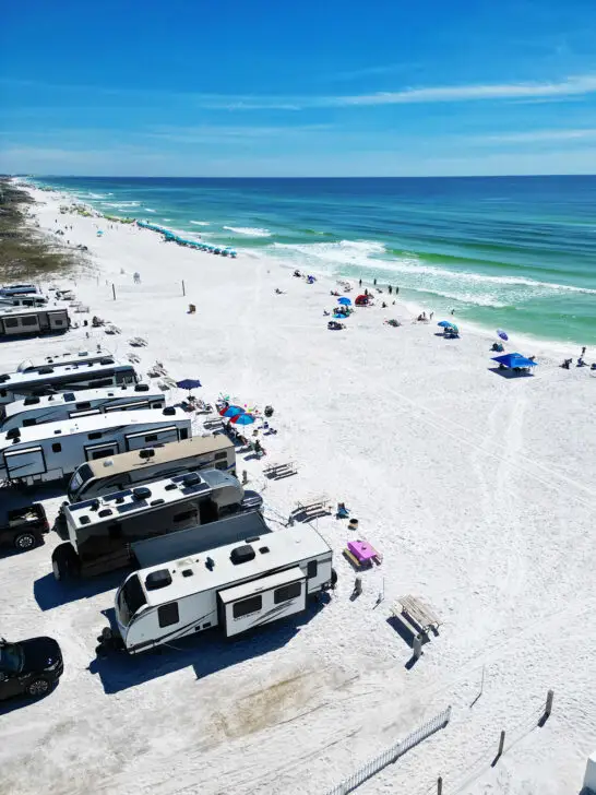 beginning rving view of campers on the beach with bright white sand and blue water